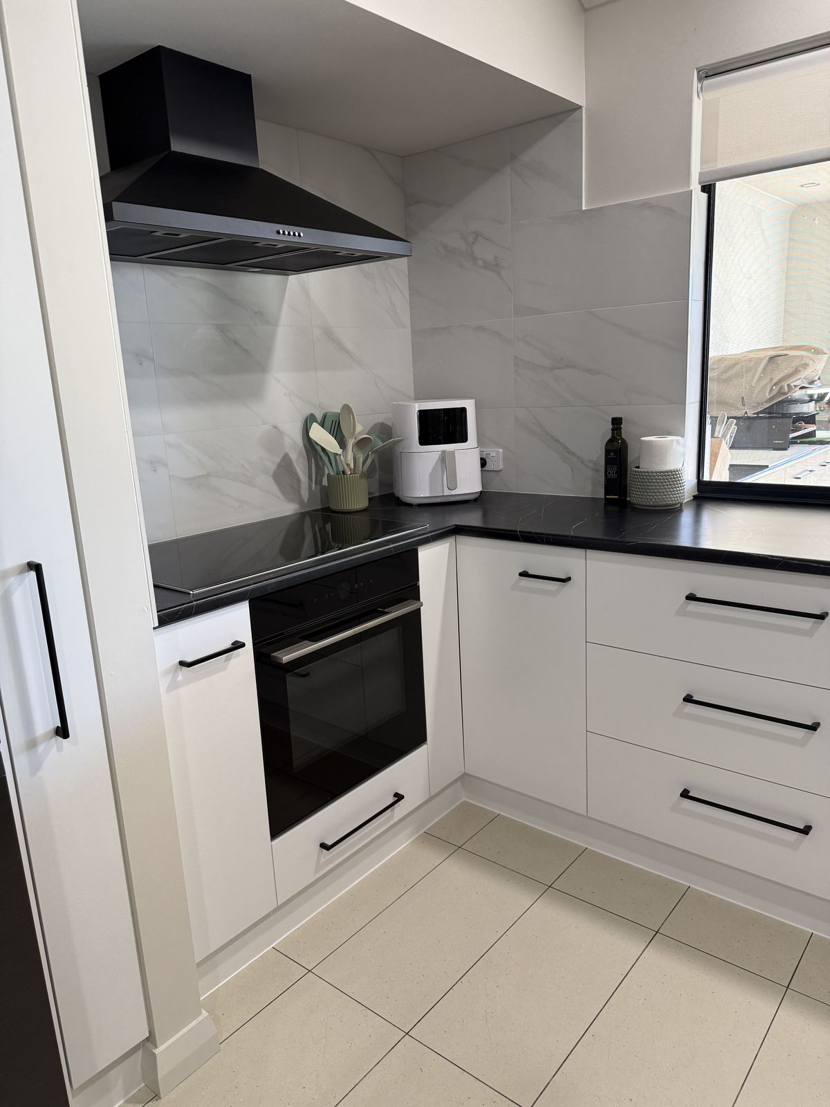 New custom kitchen with white cabinetry, black rangehood and marble splashback