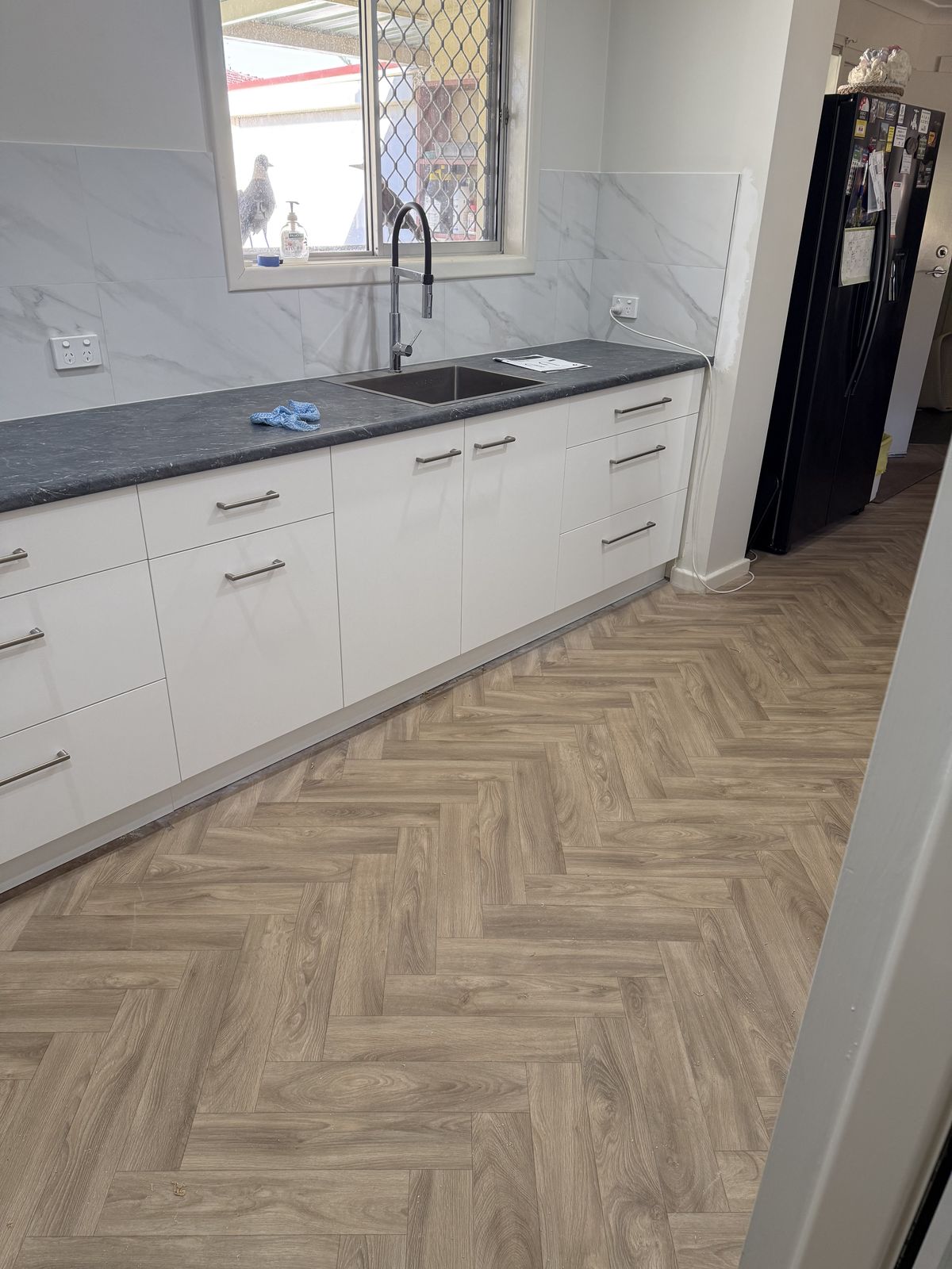 Laundry fitout with white cabinetry, stone benchtop and herringbone flooring
